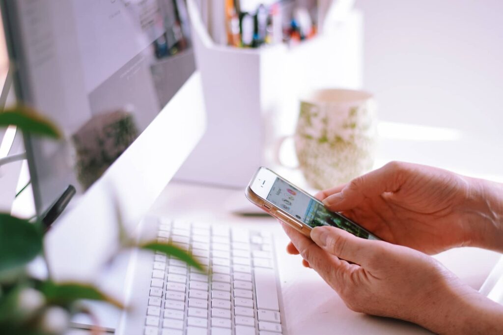 Woman typing on phone besides her desktop.