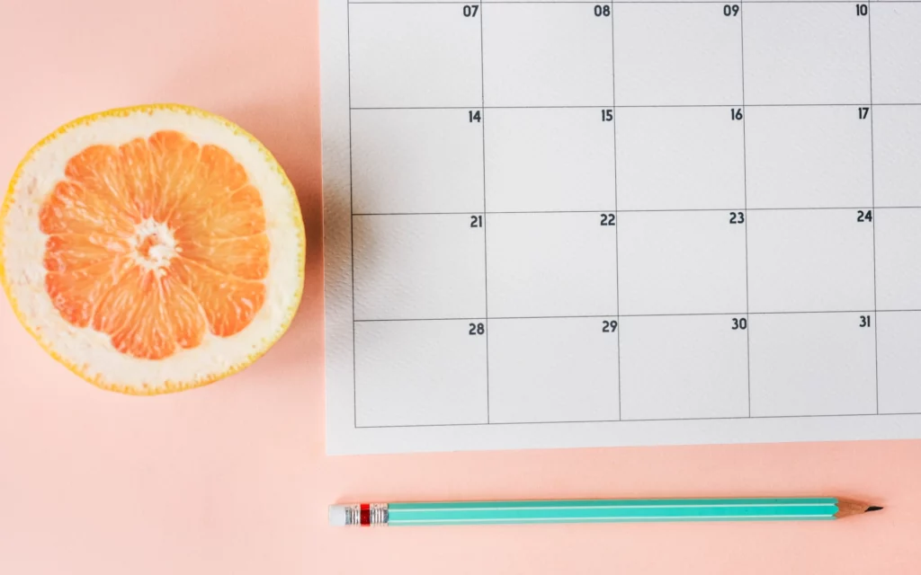 Empty calendar next to an orange slice and a pencil.