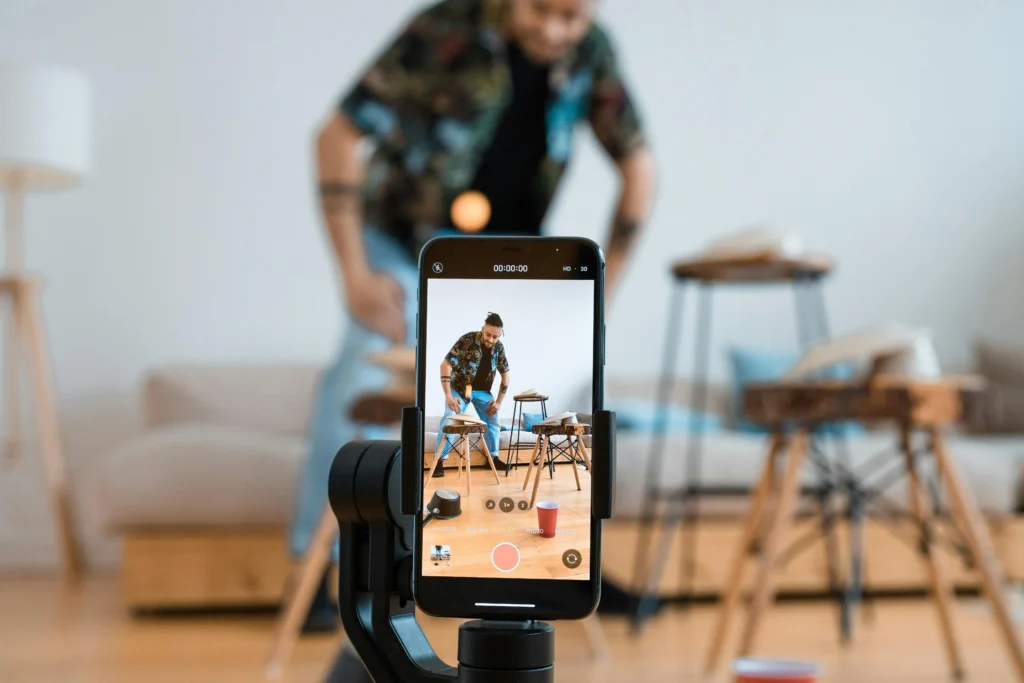 Content creator recording a video with a smartphone on a tripod, preparing social media content at home.