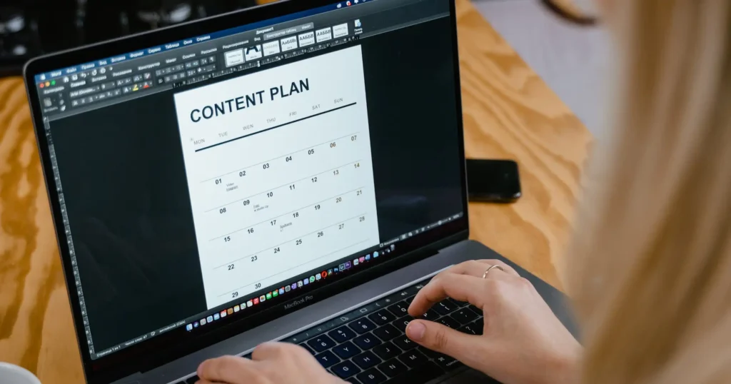 Person creating a content plan on a laptop, organizing social media posts and strategy calendar.
