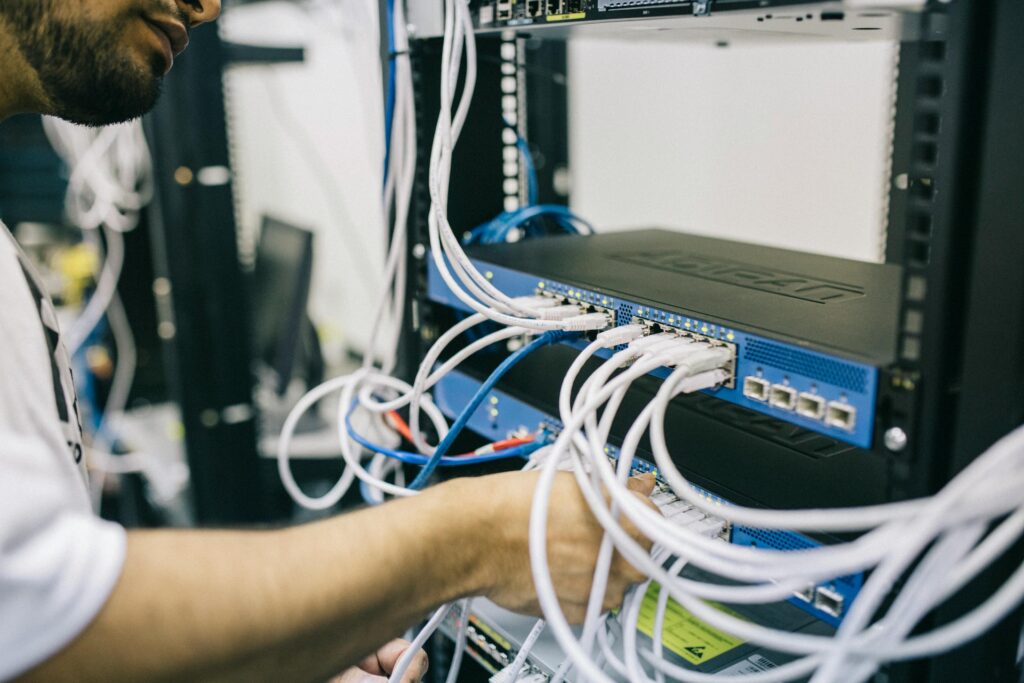 IT technician connecting ethernet cables to network switches in a server rack, configuring enterprise networking equipment in a data center, representing network infrastructure setup, cybersecurity management, and cloud computing hardware maintenance.