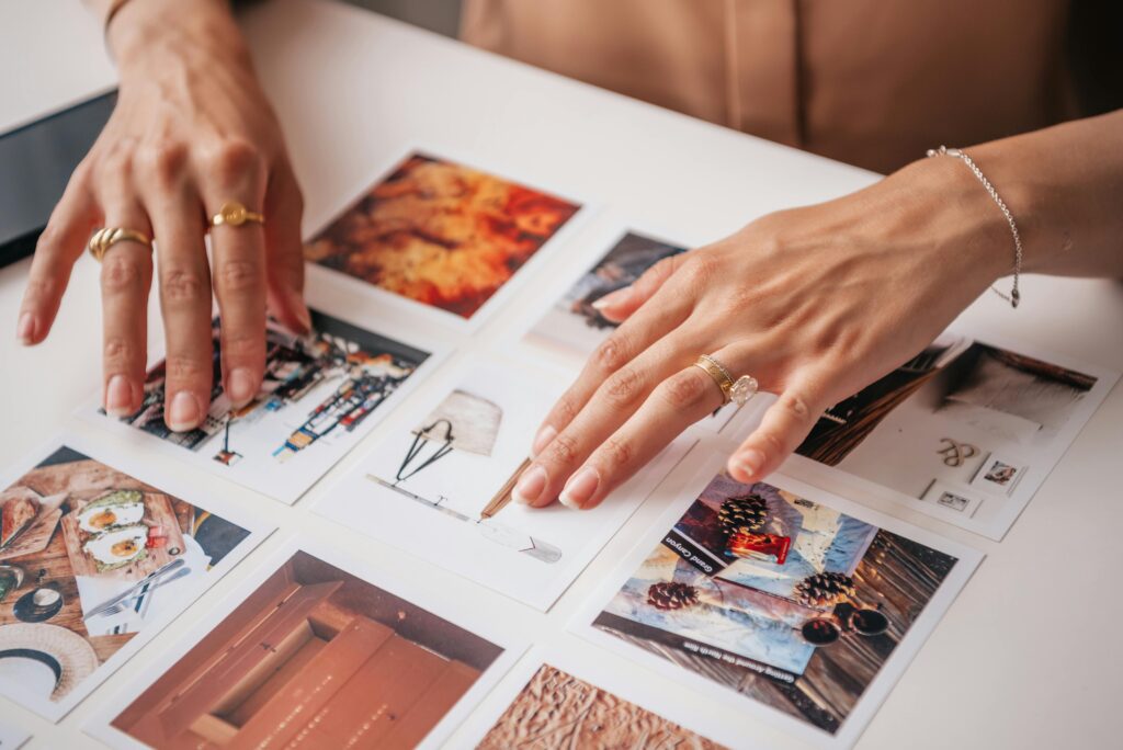 Alt text: Hands arranging printed photos on a table while planning a visual content layout, representing visual content strategy, social media content planning, and creative content organization for marketing.