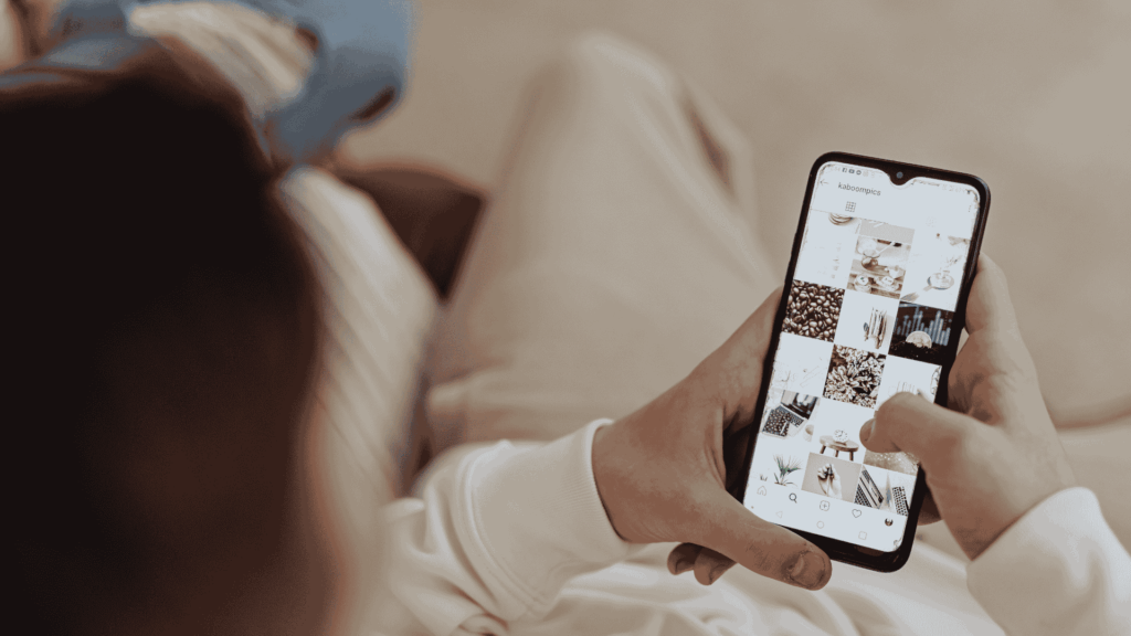 Person holding a smartphone and browsing an Instagram-style photo grid while sitting indoors in a relaxed setting.
