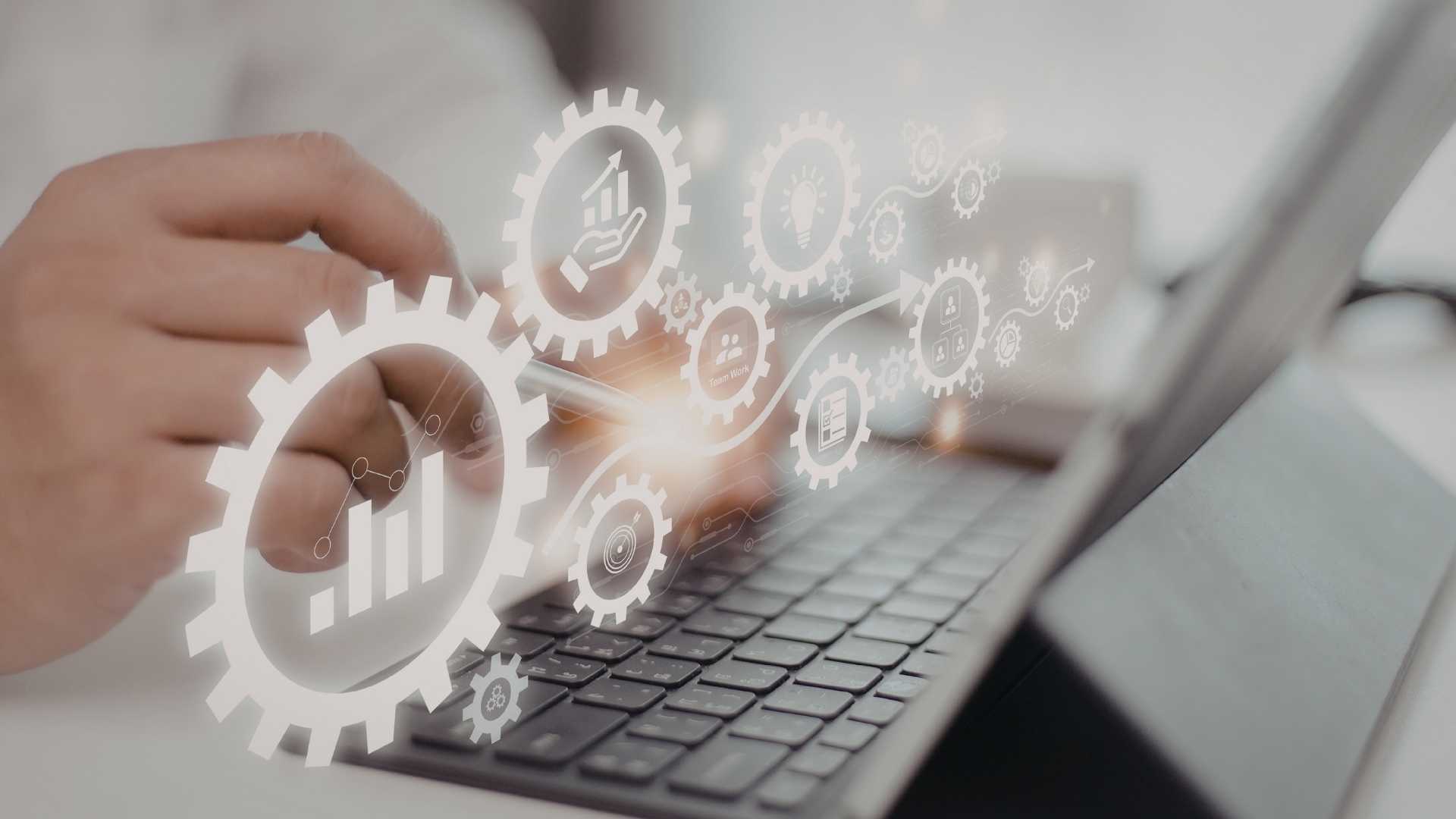 Hand using a tablet keyboard with translucent gear and analytics icons overlayed.