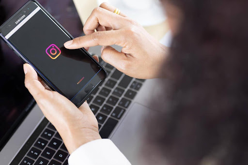 Person holding a smartphone with the Instagram logo on screen above a laptop keyboard