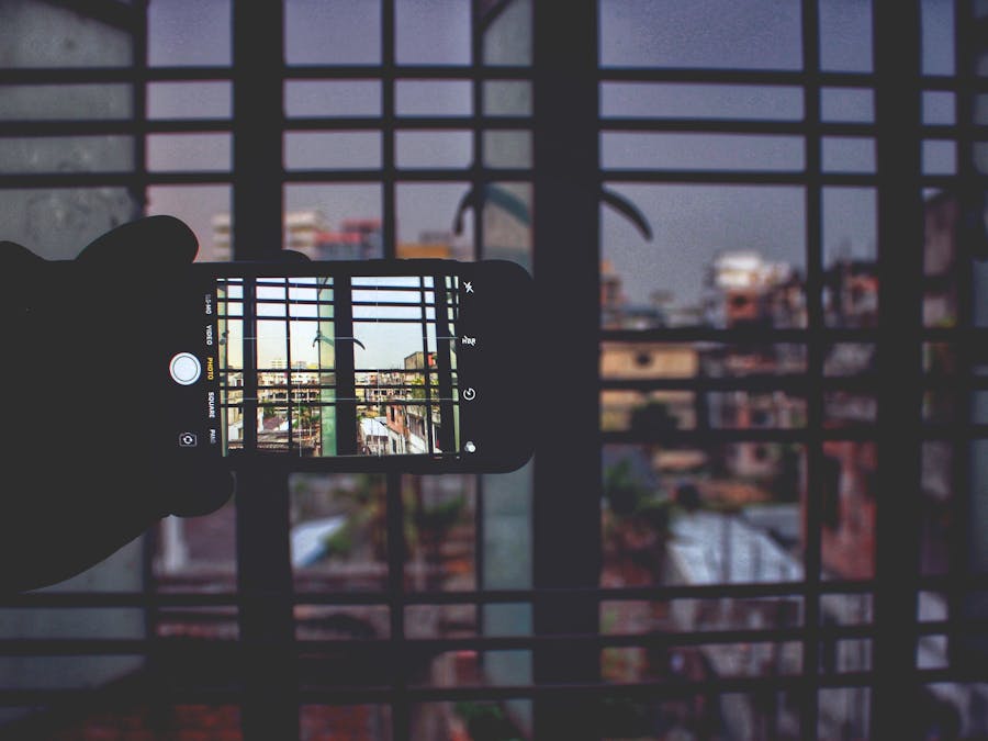 Urban scene captured through a smartphone framed by window bars, creating a modern, abstract composition.