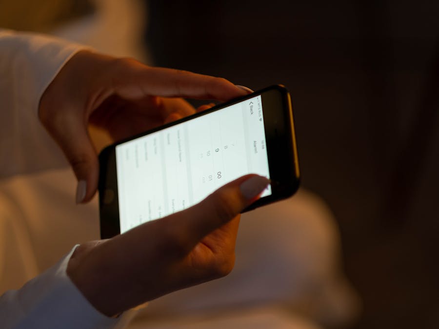 Close-up of hands setting an alarm on a smartphone, depicting night usage and technology interaction.