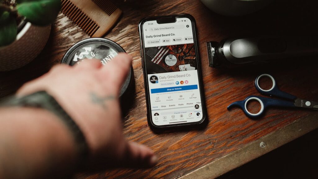 Barber tools and a smartphone showing a grooming brand site on a wooden table.