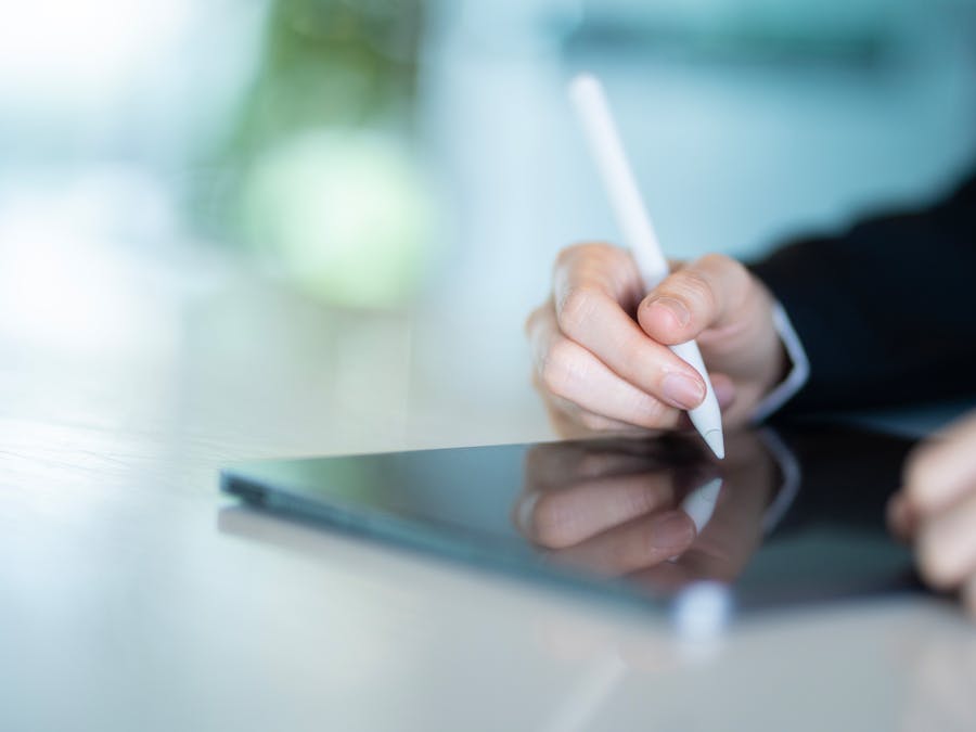 Close-up of a hand using a stylus on a tablet in a modern office, depicting digital work and productivity.