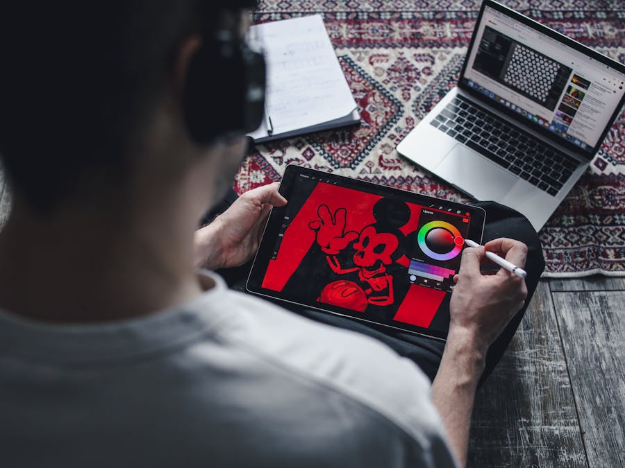 A person drawing on a tablet with a laptop nearby, showcasing digital art creation at home.