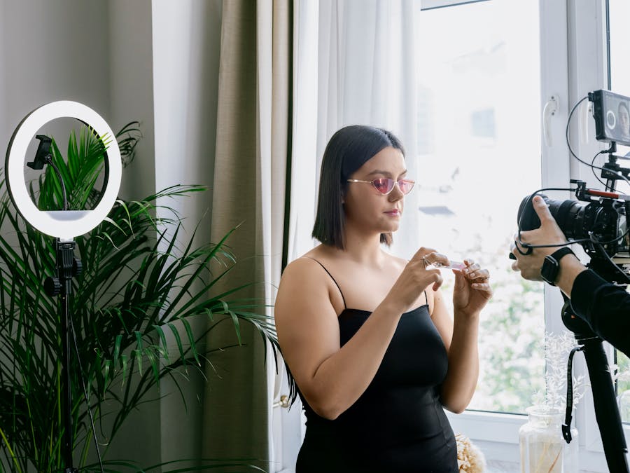 Woman filming a product review indoors with a camera and ring light.