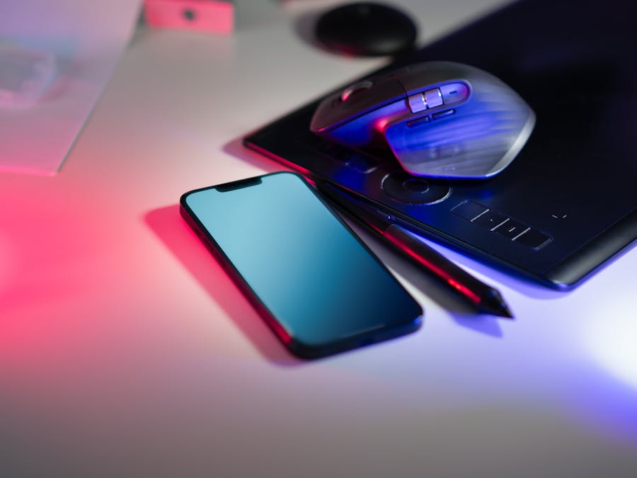 Modern workspace featuring a stylus tablet, smartphone, and computer mouse under colorful lighting.