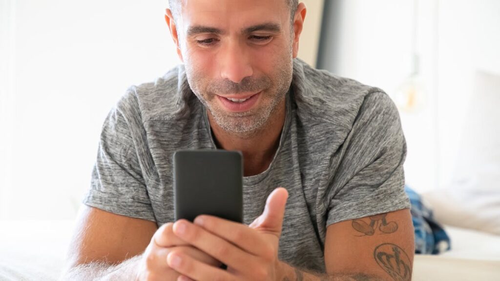 Adult man using smartphone comfortably indoors, conveying modern lifestyle.