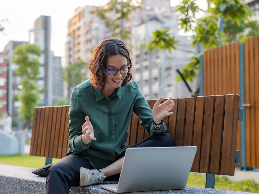 Smiling woman video calling with laptop outdoors on a sunny day.