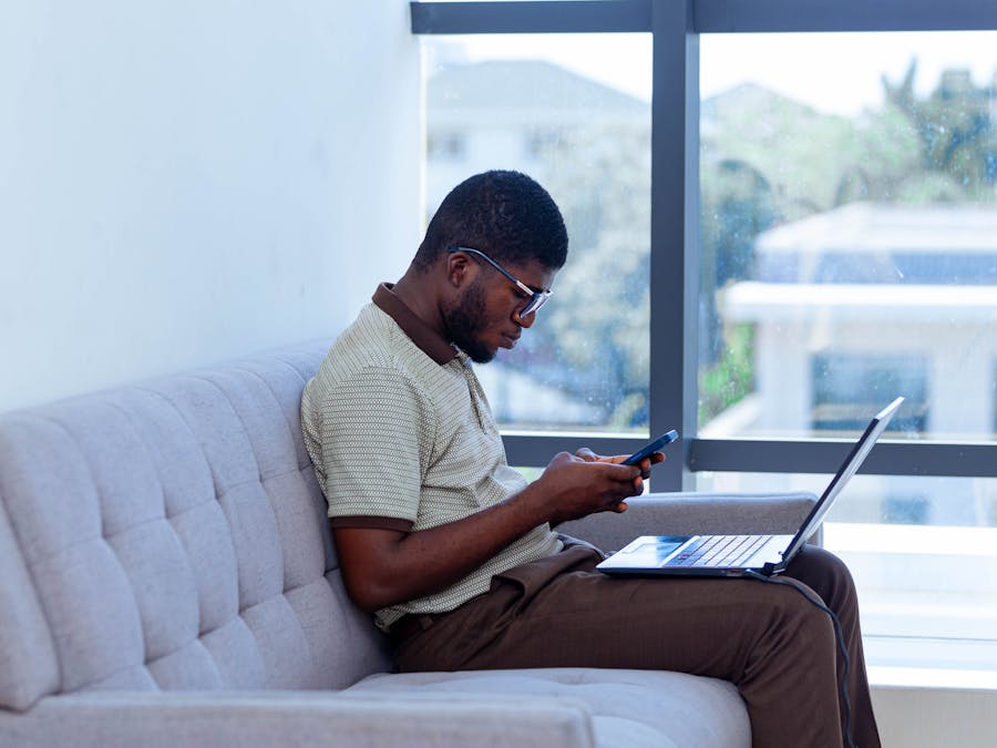 Man multitasking with laptop and smartphone indoors, showcasing remote work lifestyle.