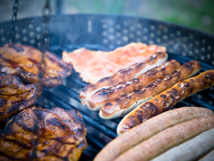 Close-up of various meats including sausages grilling outdoors on a barbecue.