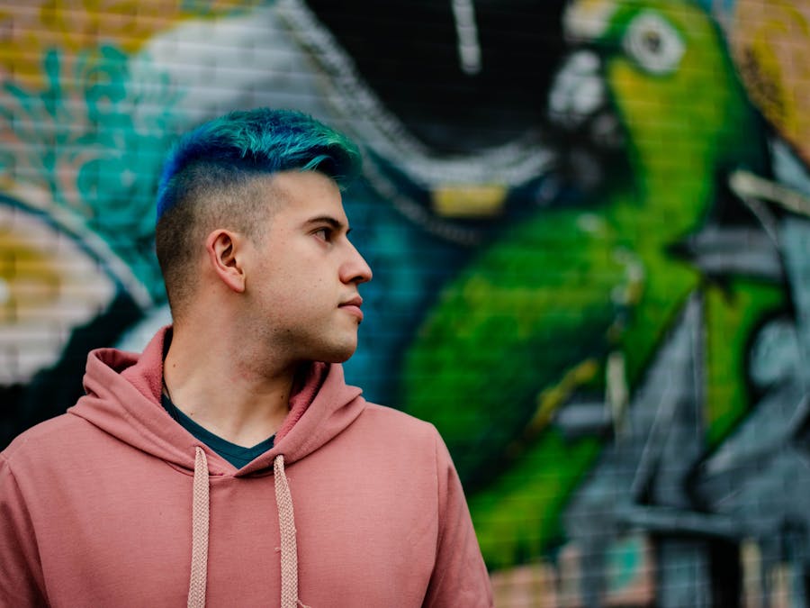 Urban portrait of a young man with vibrant blue hair against a colorful graffiti wall.