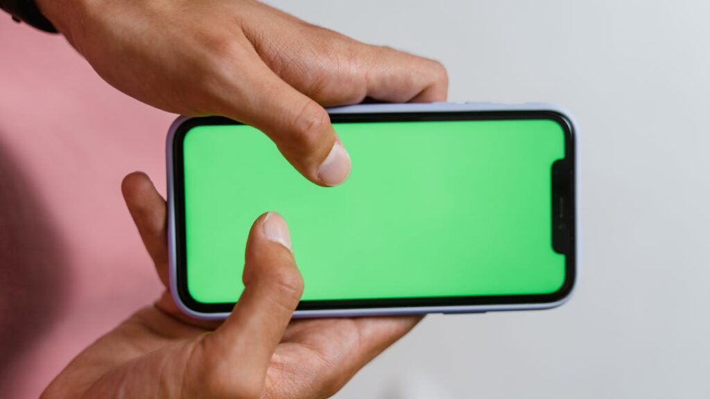 Hands holding smartphone with a green screen, suitable for digital content overlay.