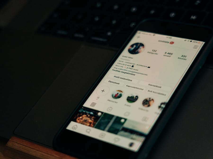 Close-up of smartphone showing a social media profile screen next to a laptop.