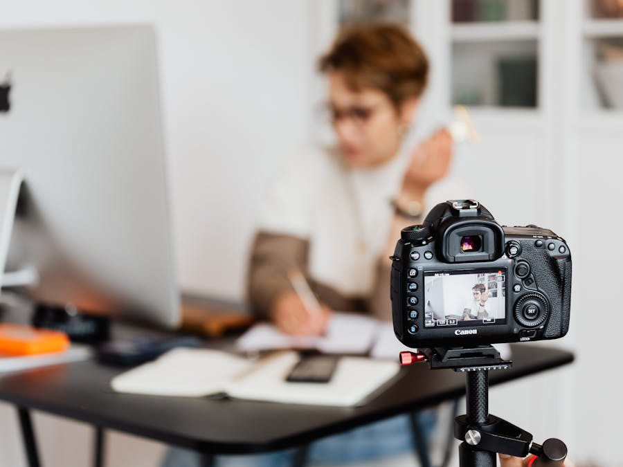 Unrecognizable blurred lady working at table in modern office against photo camera placed on tripod