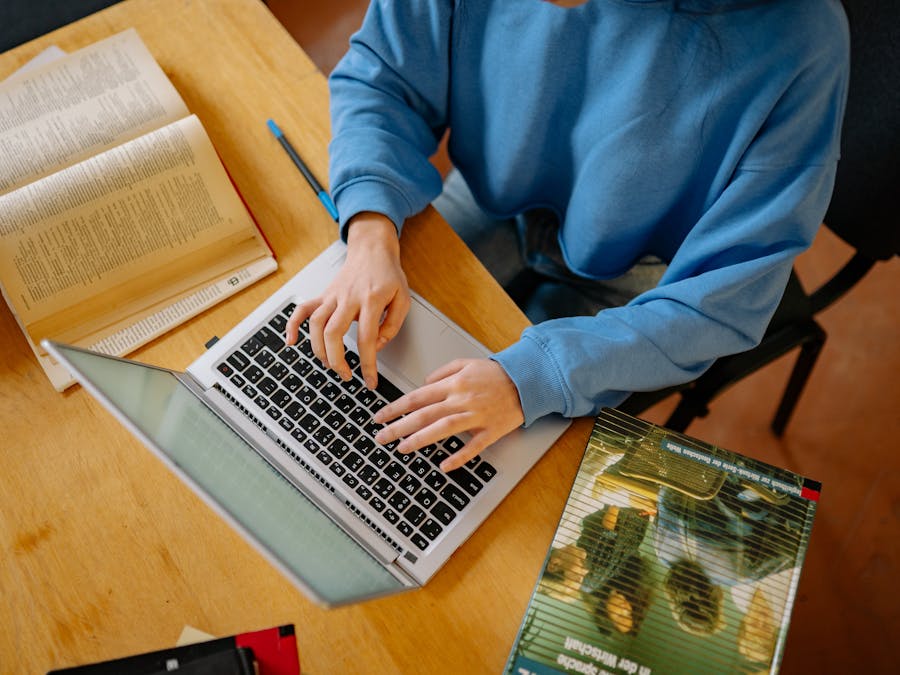 A student typing on a laptop surrounded by open books, focusing on research and school work.