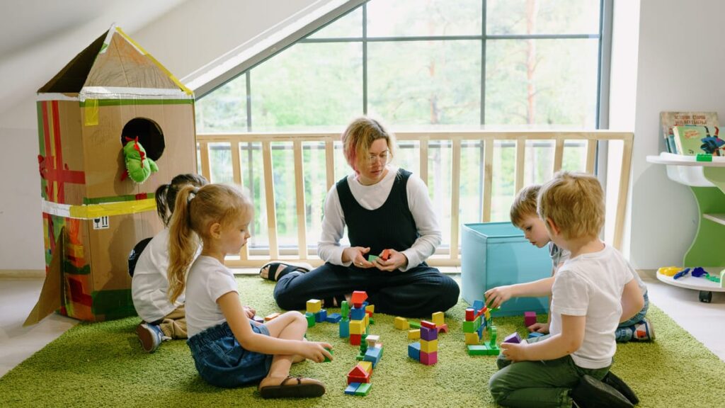 Children enjoying playtime with blocks and cardboard house in a cozy classroom.