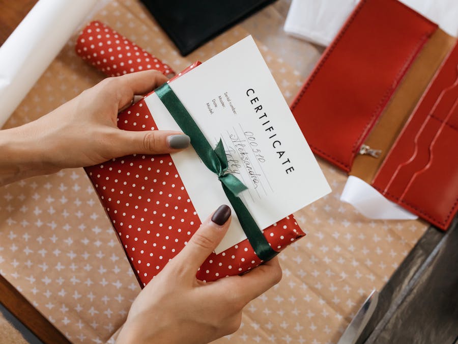 Close-up of hands holding a gift certificate wrapped in red polka dot paper and green ribbon.