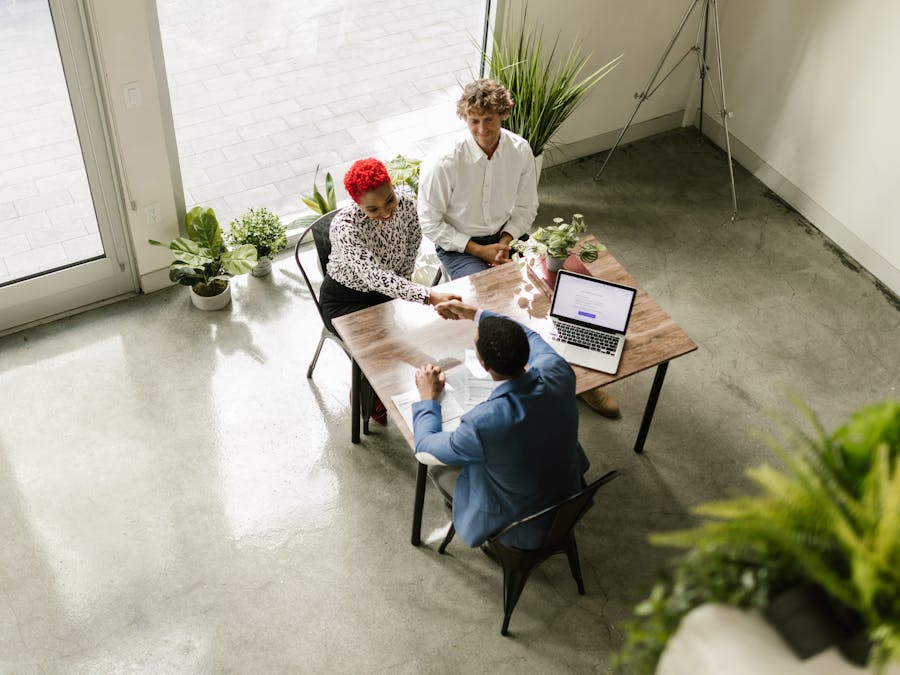 A high-angle view of professionals having a meeting in a modern office setting, shaking hands over a table.