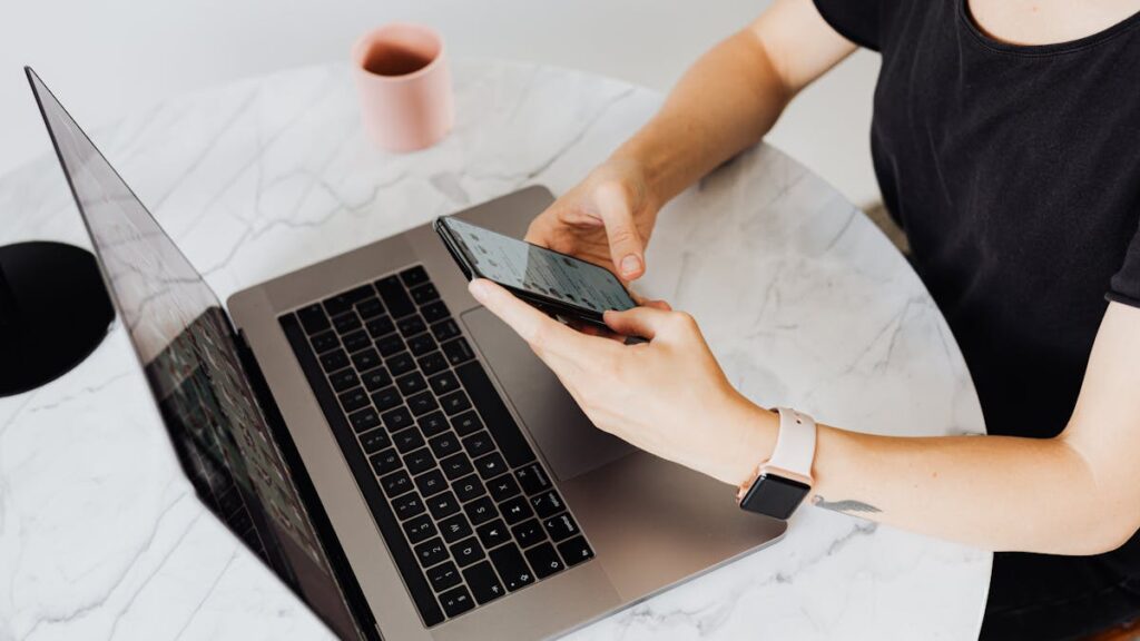 A woman interacts with her smartphone at a modern desk with a laptop, showcasing technology use.