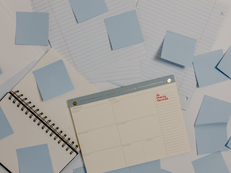 Top view of a desk with planner, sticky notes, and lined papers for organization.
