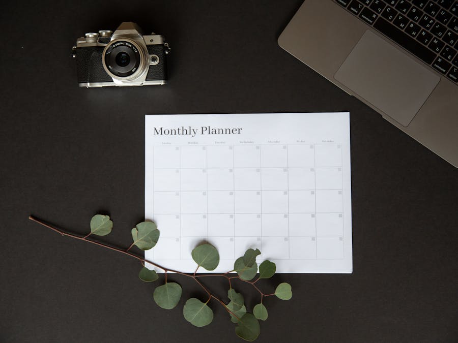 Flat lay of a monthly planner beside a camera and laptop for productivity.