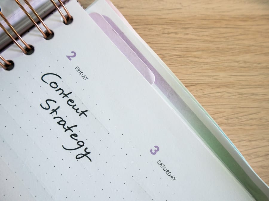 Top view of a notebook open to a day planner featuring 'Content Strategy' handwritten, lying on a wooden desk.