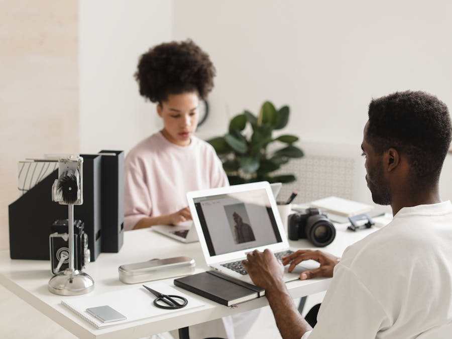 Two creative professionals collaborating in a bright, modern office setting with laptops and camera equipment.