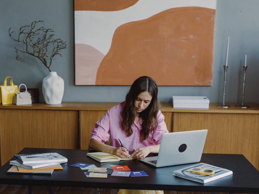 Woman working remotely at home office on a design project with laptop and color swatches.