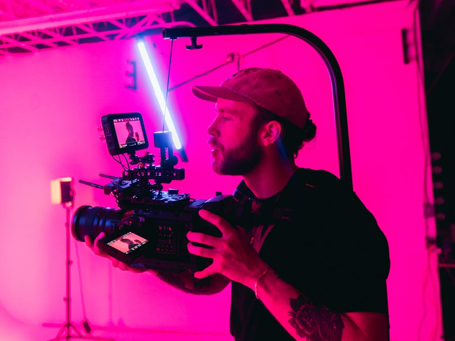 Bearded videographer in a neon-lit studio filming with professional camera setup.