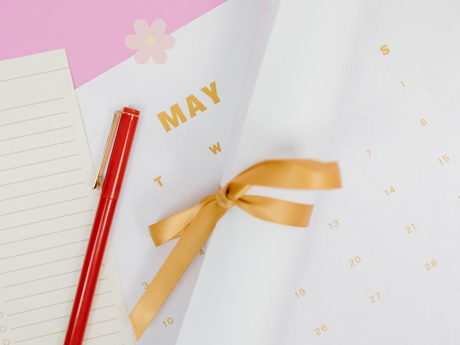 A minimalist flat lay of a calendar with red pen and ribbon on a pink background, perfect for planning.