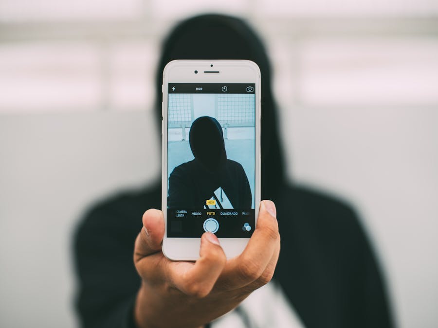 A person in a hoodie takes a mysterious selfie with a smartphone.