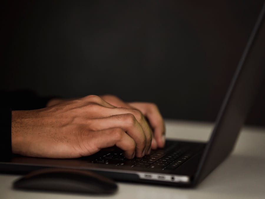 Crop unrecognizable person surfing internet on contemporary netbook and typing on keyboard in dark workspace