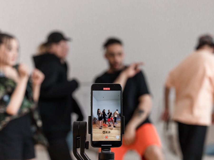 Group of dancers recording performance with smartphone on tripod, capturing trendy dance moves.