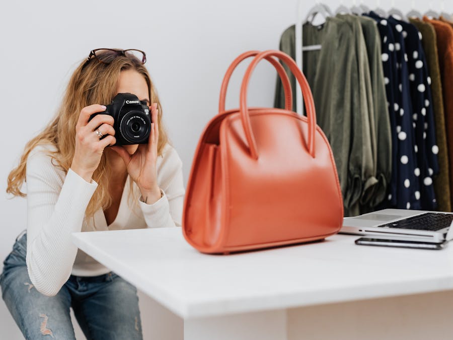 Caucasian woman capturing handbag photos for online fashion retail with camera.