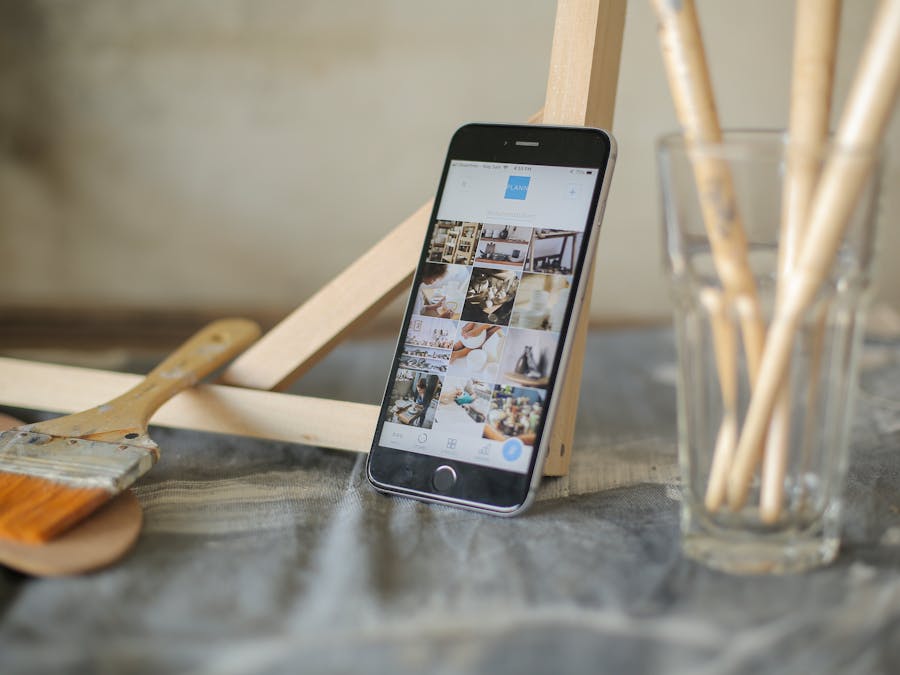 Modern smartphone displaying images amidst artist brushes and easel.