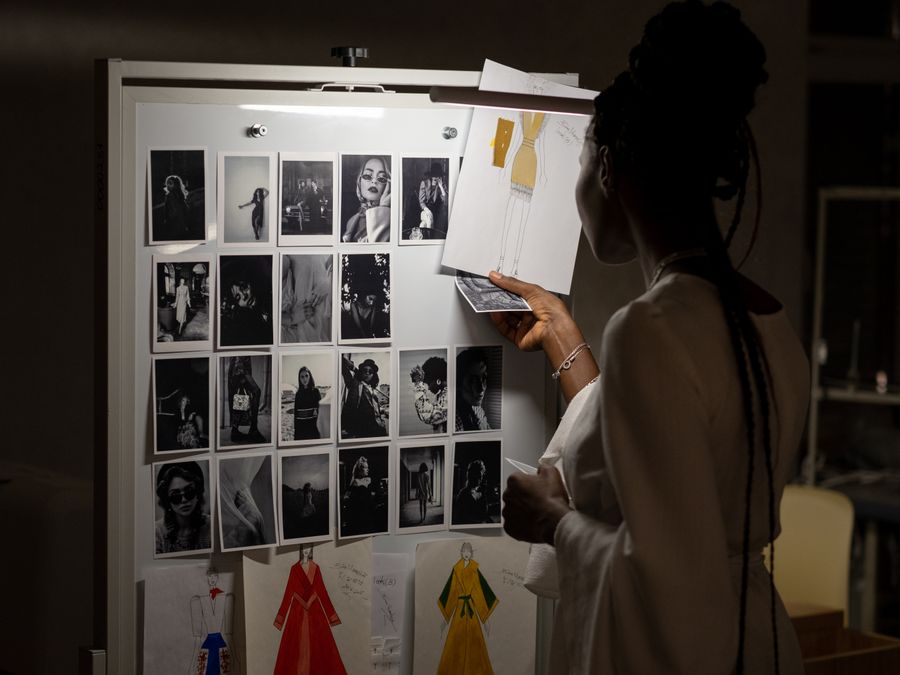 A fashion designer evaluating sketches and photos on a workspace board.