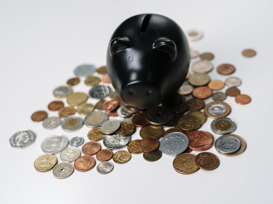 Black piggy bank surrounded by a variety of coins on a white surface, symbolizing savings and finance.