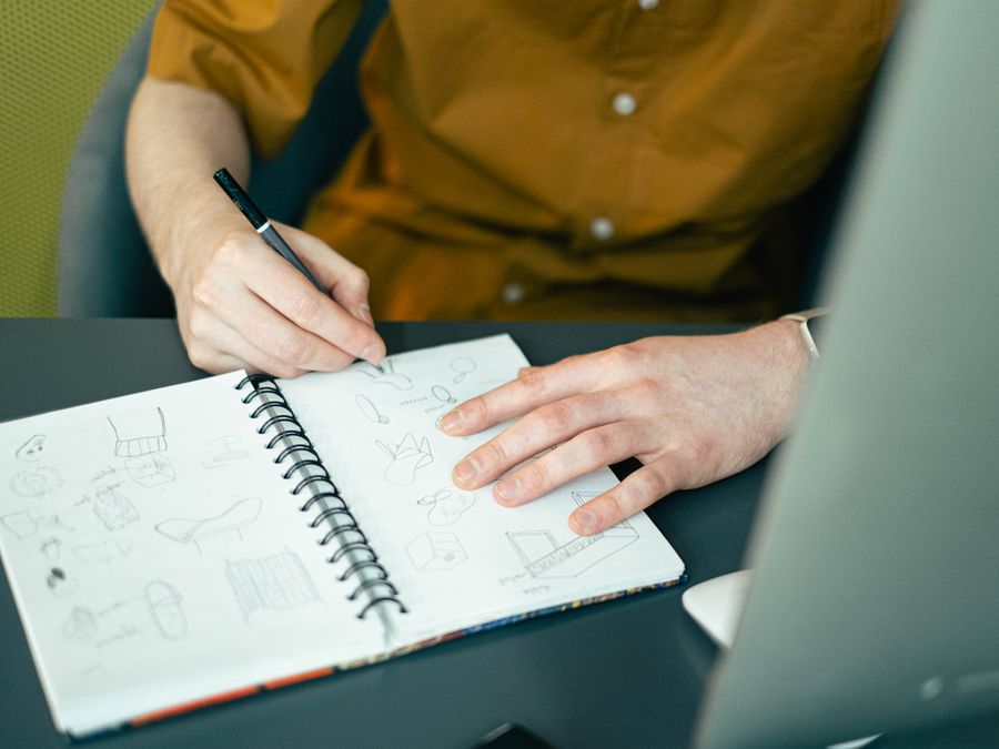 Close-up of a designer sketching ideas in a spiral notebook at a desk, highlighting creativity.