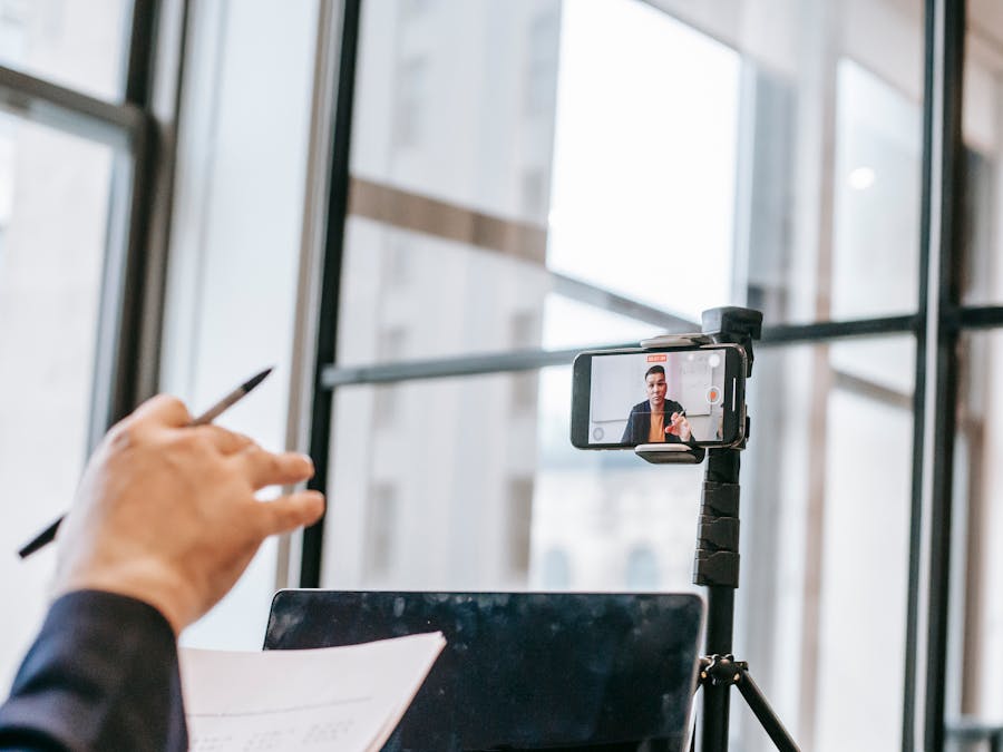 A professional conducting an online class using a smartphone camera on a tripod indoors.