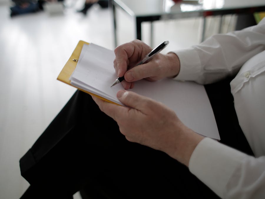 Side view crop male executive in formal wear writing on paper placed on clipboard while working on project in contemporary workplace