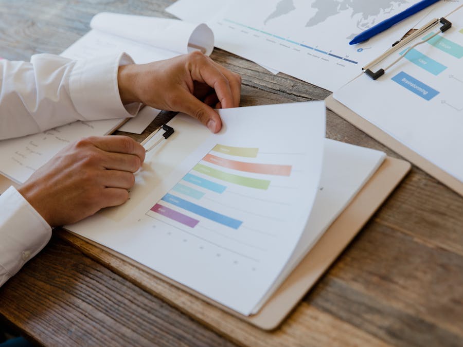 Close-up of hands reviewing business report with colorful charts and graphs on a wooden desk.