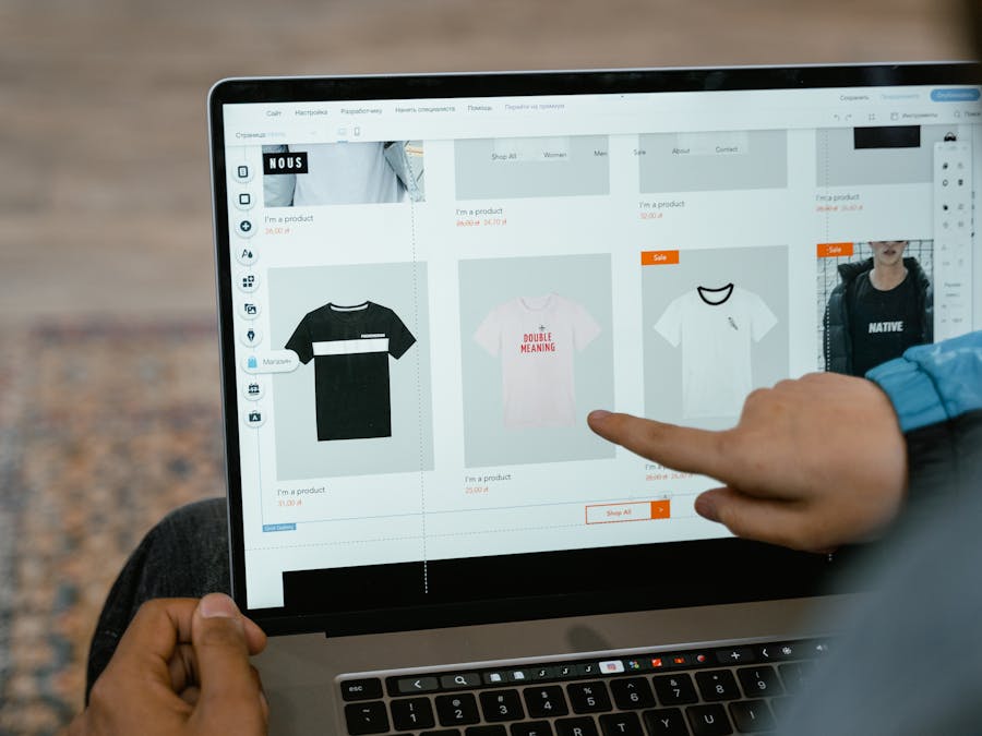 A person points to t-shirt options in an online store on a laptop screen.