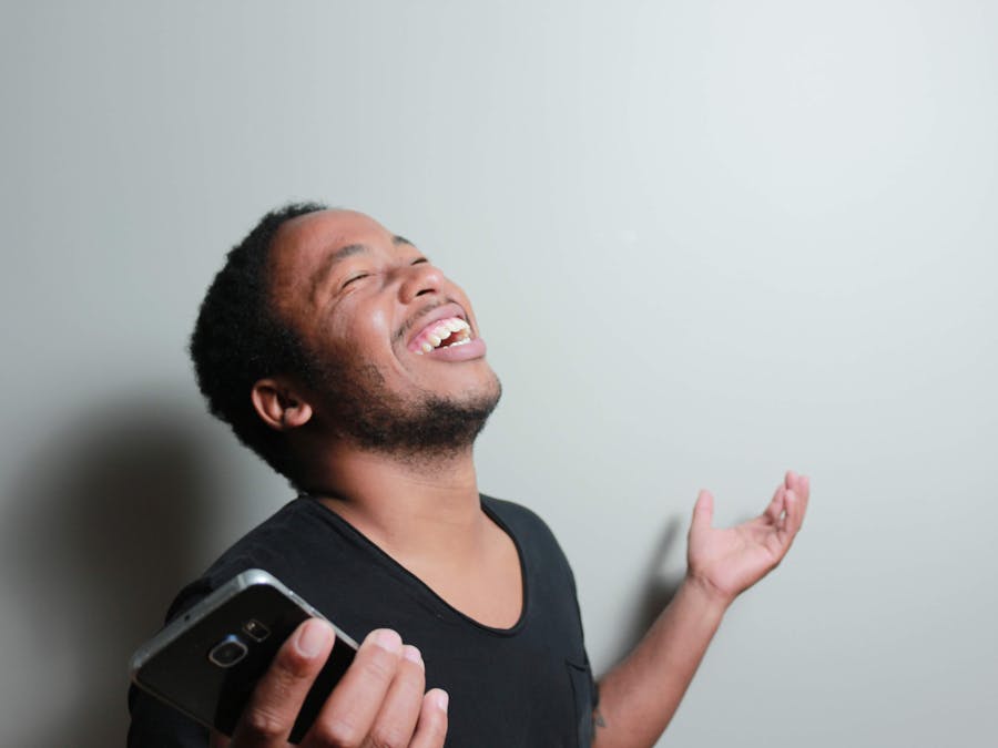 A cheerful man joyfully expresses happiness while holding a smartphone indoors.
