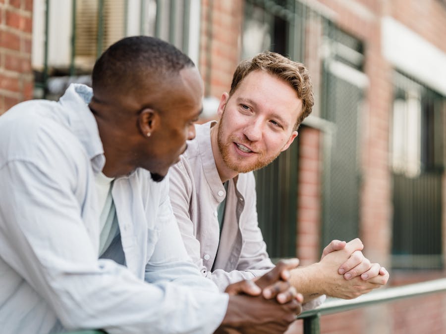 Two men engaging in lively conversation outdoors against a brick wall background.